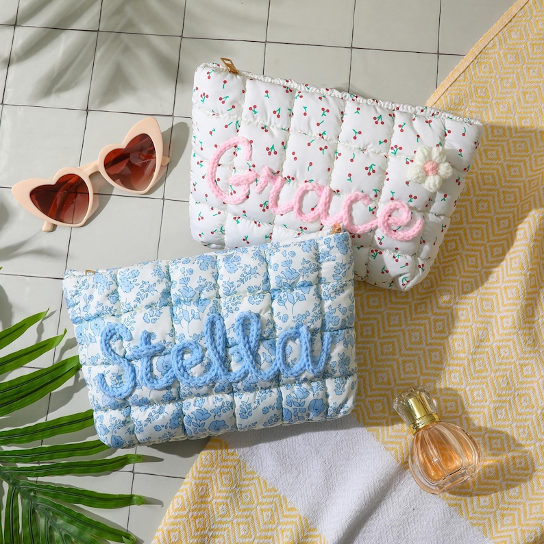 May include: Two quilted cosmetic bags, one white with a cherry print and the name "Grace" in pink, the other blue floral with "Stella" in blue. Heart-shaped sunglasses and a perfume bottle are also visible.