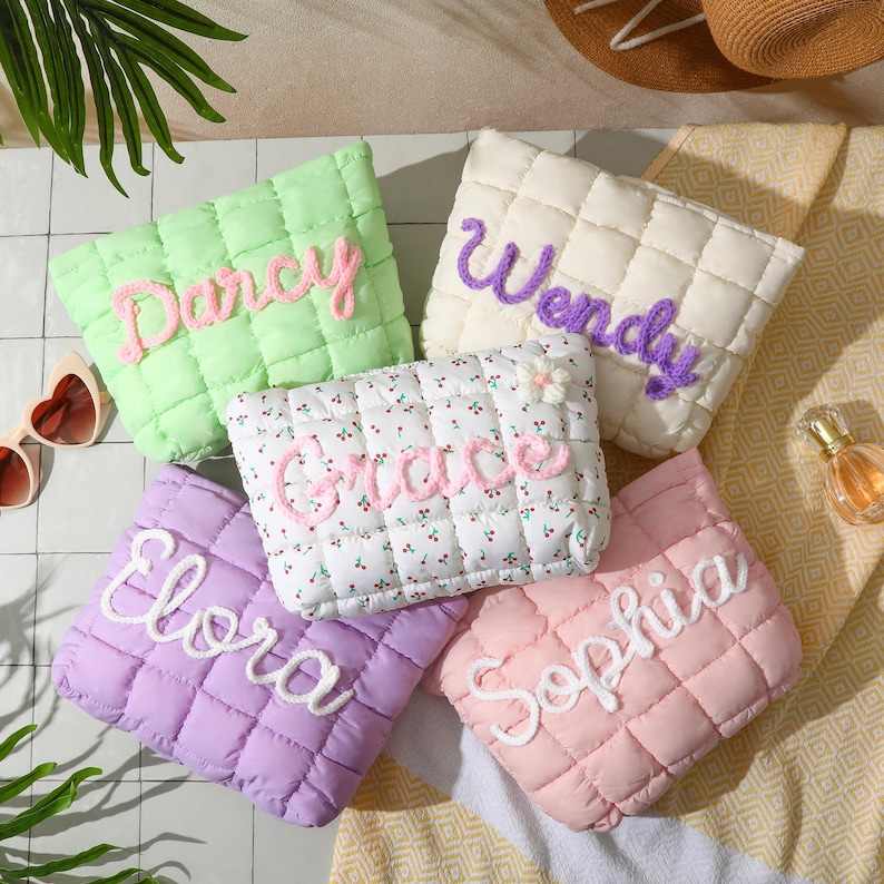 May include: Five quilted pouches in pastel shades, each embroidered with a different name: Darcy, Wendy, Grace, Elora, and Sophia. The pouches feature a diamond pattern and are arranged on a patterned surface, ideal for a personalised gift.