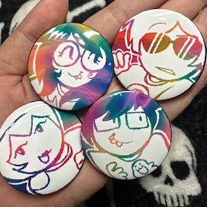 May include: Four round white buttons with cartoon character designs. Each button features a different character outline in rainbow colors against a white background. The characters have various expressions and wear glasses or sunglasses.