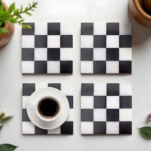 Peut inclure: Quatre dessous de verre carrés avec un motif en damier noir et blanc. L'un d'eux supporte une tasse blanche remplie de café noir. Les dessous de verre sont en matériau semblable au marbre, disposés sur une surface blanche.
