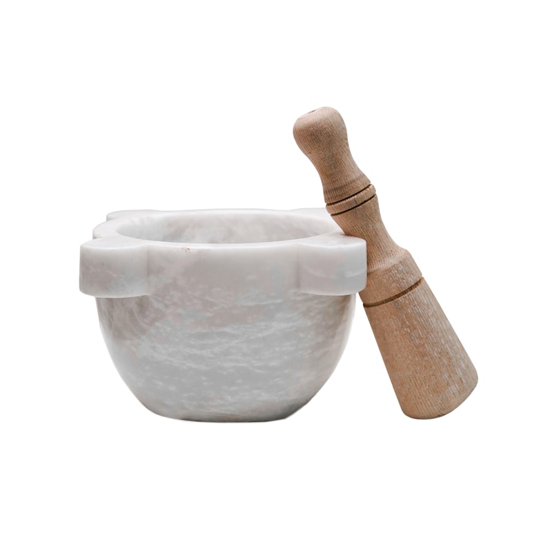 May include: A white marble mortar and pestle set. The mortar has a scalloped rim and a rounded bowl. The pestle is made of light-colored wood. This kitchen tool is ideal for grinding herbs and spices.