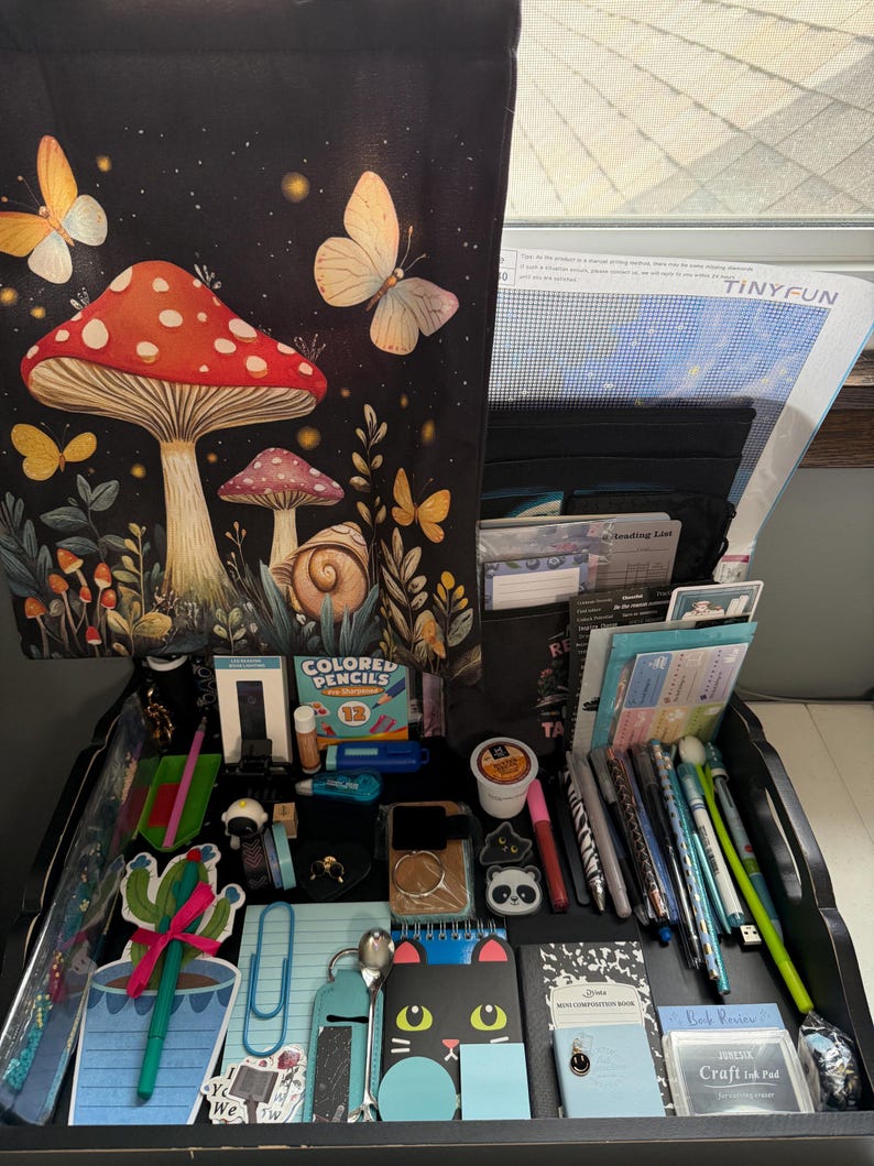 Peut inclure: Un plateau organisateur noir rempli de fournitures de papeterie, incluant une housse en tissu &agrave; motifs de champignons et papillons, un kit de broderie diamant TinyFun, des crayons de couleur, des stylos, un bloc-notes cactus et un carnet chat noir.