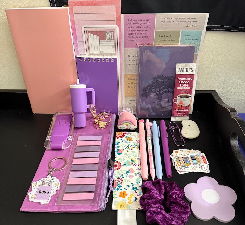 Peut inclure: Un ensemble de papeterie comprenant un carnet rose, un bloc-notes &agrave; spirales violet, un gobelet violet, un sachet de Maud's Raspberry Choco-Latte, des stylos, un marque-page floral, un chouchou violet, un post-it en fleur et divers autocollants.