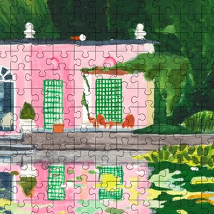 May include: A completed jigsaw puzzle featuring a pink building with green shutters and a black roof. The building has a white trim and is surrounded by green foliage. The puzzle has a watercolor painting style.