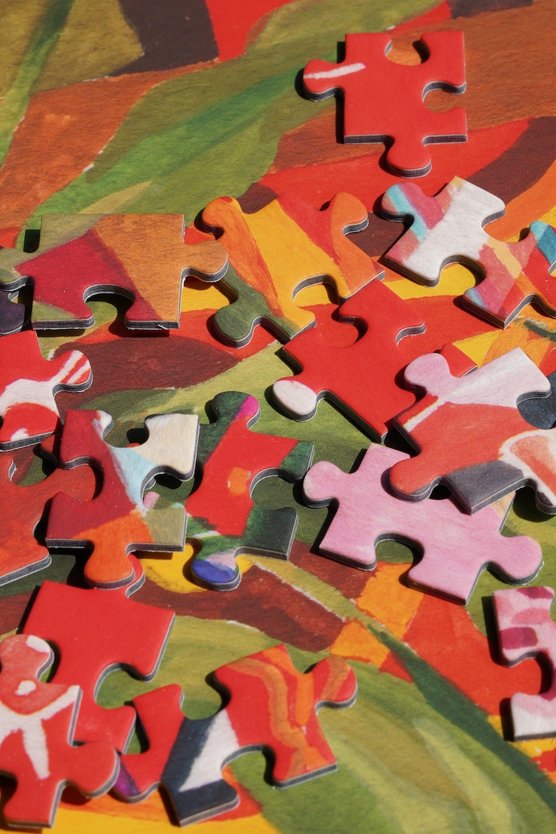 May include: Close-up of a partially assembled jigsaw puzzle. The puzzle pieces are primarily red, with accents of pink, yellow, and white. The background features a colorful abstract design with green, orange, and brown hues. A fun activity for all ages.