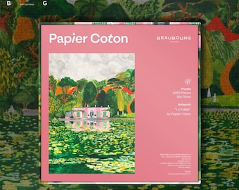 May include: A 1000-piece jigsaw puzzle with the artwork "La Folie" by Papier Coton. The puzzle box is pink and features a colorful painting of a pink building reflected in water, surrounded by lush green trees. The puzzle measures 50x70cm.