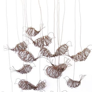 May include: A hanging mobile featuring multiple bird figures crafted from thin, brown, coiled wire. Each bird is suspended by a single wire from a circular, grid-like metal frame at the top, creating a layered, three-dimensional display of wire art.