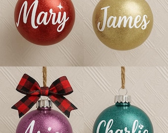 Könnte beinhalten: Vier personalisierte Weihnachtskugeln. Die Kugeln sind rot, gold, lila und türkis, jede mit einem Namen in weißer Schrift: Mary, James, Aria und Charlie. Jede Kugel hat eine andere Schleife oder ein anderes Band.