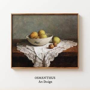 Puede incluir: Pintura enmarcada de naturaleza muerta con un cuenco de fruta amarillo-verde sobre un mantel de encaje blanco. El cuenco es blanquecino con un diseño floral azul. La pintura está sobre una mesa marrón oscuro sobre un fondo gris apagado. El texto "OSMANTHUS Art Design" está en la parte inferior.
