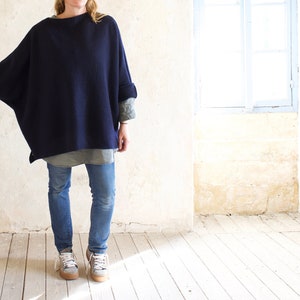 Könnte beinhalten: Ein übergroßer, marineblauer Pullover mit langen Ärmeln und lockerer Passform. Der Pullover wird über einem hellgrünen Hemd und einer blauen Jeans getragen.