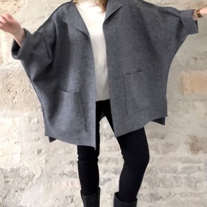 Op de afbeelding: Een grijze oversized cardigan met een lange, losse pasvorm en twee zakken. De cardigan is open aan de voorkant en heeft een kraag.