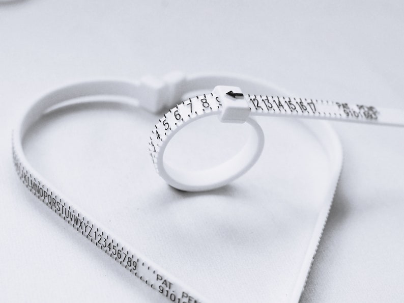 Puede incluir: Un medidor de talla de anillo de pl&aacute;stico blanco con los n&uacute;meros del 1 al 17 impresos en &eacute;l. El medidor tiene la forma de un anillo y se utiliza para medir el tama&ntilde;o de un dedo.
