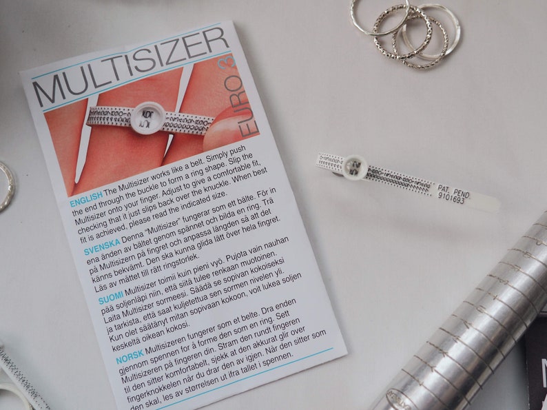 Puede incluir: Un ajustador de anillos de pl&aacute;stico blanco con marcas negras y el texto "Multisizer" y "Euro" impreso en &eacute;l. El ajustador est&aacute; dise&ntilde;ado para medir los tama&ntilde;os de los anillos y se muestra sobre una superficie blanca.