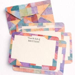 May include: A stationery set comprising an envelope and notecards, showcasing a vibrant geometric design. The envelope and card edges display a mosaic pattern in purple, orange, blue, and green hues. The notecards are inscribed with the text "From the desk of BRITTANY".