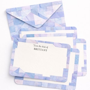 Op de afbeelding: Briefpapier set met een envelop en notitiekaarten. Het ontwerp is een geometrisch aquarelpatroon in blauwe en paarse tinten. De notitiekaarten hebben de tekst "From the desk of BRITTANY".
