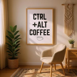 Pode incluir: Uma impressão emoldurada com as palavras "CTRL + ALT COFFEE" em preto, com uma ilustração de xícara de café. A impressão está pendurada em uma parede bege, acima de uma poltrona bege e uma mesa lateral de madeira.