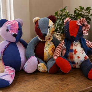 May include: Three stuffed teddy bears made from various fabric patches. The left bear is purple and tie-dye. The center bear features denim, maroon, and sunflower patterns. The right bear has red, blue, star-patterned fabric, and a gingham bow.