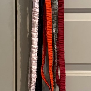May include: A collection of six colorful lanyards hanging from a silver door handle. The lanyards are in various colors, including pink, black, orange, gray, and red. Each lanyard has a silver clasp and key ring.