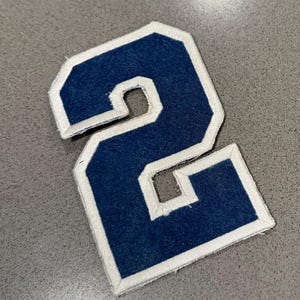Puede incluir: Parche de fieltro azul marino con el número 2 y borde blanco. El parche tiene un estilo clásico de letra universitaria, perfecto para chaquetas, bolsos u otros proyectos de manualidades. El número está en negrita.