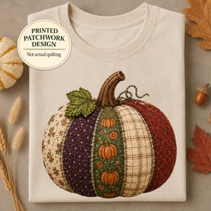 May include: A cream-colored t-shirt featuring a large graphic of a pumpkin with a printed patchwork design. The pumpkin is composed of various fabric patterns including floral, polka dot, and plaid textures in shades of orange, green, and red.