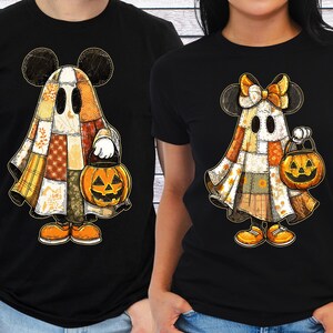 May include: Black t-shirts featuring a Halloween-themed design. The design includes a ghost character with Mickey Mouse ears, a patchwork-style costume, and a jack-o'-lantern. The ghost is holding a pumpkin-shaped treat bucket. The design is in shades of orange, yellow, and brown.