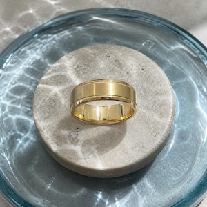 Puede incluir: Un anillo de banda de oro con un acabado central cepillado y liso, bordeado por finos bordes pulidos con una delicada textura milgrain. El anillo tiene un perfil ancho y clásico con una superficie interior brillante y un tono de oro amarillo.