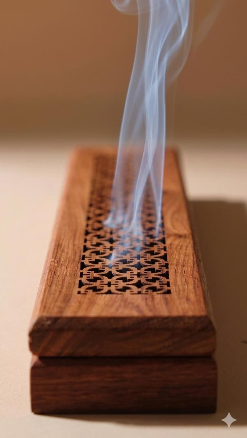 May include: A rectangular wooden incense burner with a carved geometric design. Wisps of white smoke rise from the top. The burner is made of dark brown wood.