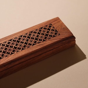 May include: A rectangular wooden box with a decorative geometric pattern carved into the lid. The box is made of a dark brown wood and has a black interior. The design is symmetrical and adds a touch of elegance.