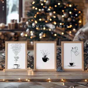 May include: Three framed art prints with coffee-themed illustrations. The prints are in light brown wooden frames and feature black and white drawings of coffee brewing and serving. The text "MEMONTE PRINTS" is above the frames.