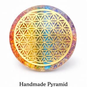 May include: A circular, handmade crystal pyramid with a gold geometric pattern. The crystal has layers of rainbow colours, including red, orange, yellow, green, blue, and purple. Text reads "Energy Protection Healing Crystal".