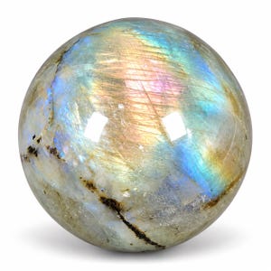 Könnte beinhalten: Ein polierter, kugelförmiger Edelstein mit einer glatten, reflektierenden Oberfläche, die irisierende Lichtreflexe in Blau, Gold und Rosa aufweist. Der Stein zeigt natürliche interne Risse und dunkle mineralische Einschlüsse.