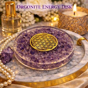 Puede incluir: Disco de energía de orgonita con un diseño dorado de la flor de la vida de Geometría Sagrada. El disco está lleno de cristales de amatista morada y se encuentra sobre una bandeja de mármol. Una vela encendida y un frasco de perfume están en el fondo.