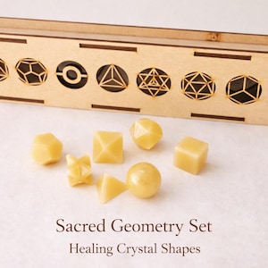 Puede incluir: Una caja de madera con recortes geométricos y un conjunto de formas de cristal amarillas. La caja tiene varios diseños geométricos. Las formas de cristal incluyen cubos, pirámides y esferas. El texto en la imagen dice "Sacred Geometry Set Healing Crystal Shapes."