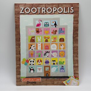 May include: A quilt pattern titled ZOOTROPOLIS by Sassafras Lane Designs featuring a gray building facade with multiple windows, each containing a different colorful animal illustration, including a flamingo, owl, panda, and penguin.