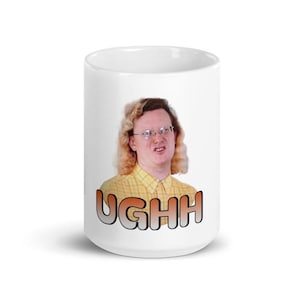 Puede incluir: Taza de cerámica blanca con una persona con gafas y la palabra "UGHH" en degradado naranja y negro. La persona lleva una camisa amarilla a cuadros.