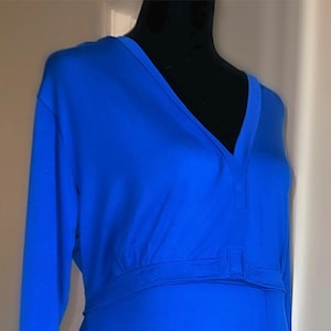 May include: A long, royal blue dress with long sleeves. The dress features a V-neckline and a fitted waist with a horizontal band. The fabric drapes smoothly, creating a flowing silhouette. The dress is displayed on a black mannequin.