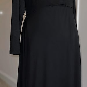 May include: A long black dress with long sleeves. The dress has a V-neckline and a fitted bodice that flows into a flared skirt. The dress is displayed on a black mannequin.