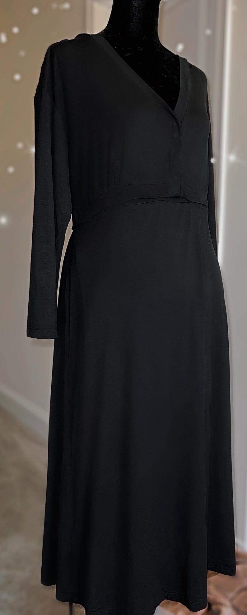 May include: A long black dress with long sleeves. The dress has a V-neckline and a fitted bodice that flows into a flared skirt. The dress is displayed on a black mannequin.