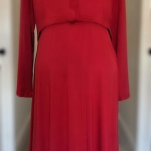 May include: A long, red dress with long sleeves and a V-neckline. The dress has a button closure at the bust and a flowing skirt. The dress is displayed on a black mannequin.