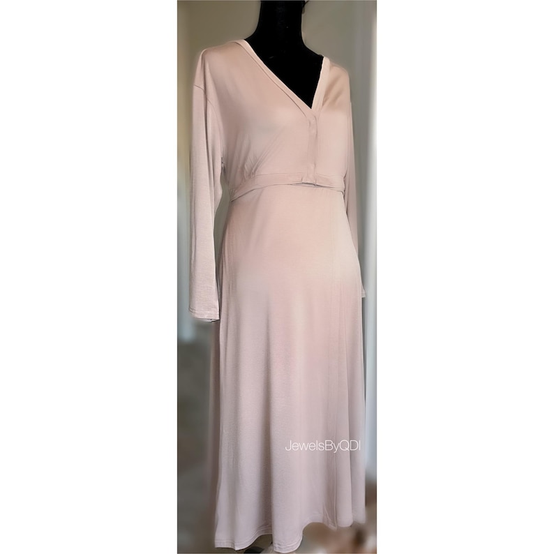 May include: A long, pale pink dress with long sleeves and a V-neck. The dress has a fitted bodice and a flowing skirt. The text "JewelsByQDI" is visible on the lower right side of the dress.