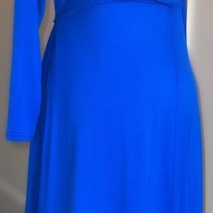 May include: A long, royal blue dress with long sleeves and a V-neck. The dress has a fitted waist and a flowing skirt. The fabric appears to be a soft, stretchy material. The dress is displayed on a black mannequin.