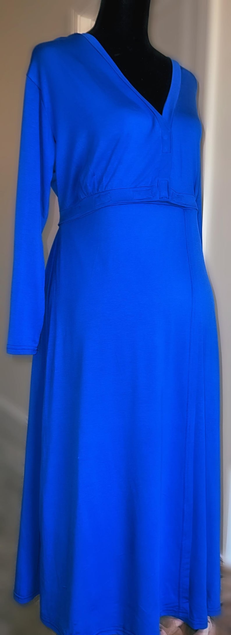 May include: A long, royal blue dress with long sleeves and a V-neck. The dress has a fitted waist and a flowing skirt. The fabric appears to be a soft, stretchy material. The dress is displayed on a black mannequin.