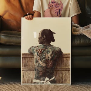 Puede incluir: Una impresión enmarcada que presenta una ilustración detallada de una persona con tatuajes tradicionales japoneses. La obra de arte representa una figura con la cabeza rapada y un intrincado arte corporal, apoyada en una estructura de madera. La impresión es sostenida por una persona.