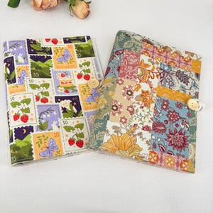 Puede incluir: Dos diarios cubiertos de tela. Uno presenta un mosaico de coloridos estampados florales, y el otro tiene un diseño de sellos con fresas, mariposas y el texto "Moonberry". Ambos tienen cierres de botón de madera.