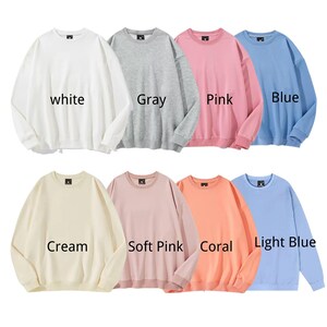 May include: A collection of eight crewneck sweatshirts in various colors: white, gray, pink, blue, cream, soft pink, coral, and light blue. Each sweatshirt has the color name printed on it.