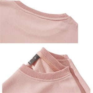 May include: Close-up of a light pink crew neck sweatshirt. The neckline and cuffs are ribbed. The tag is visible, with the size XL. The fabric appears soft and comfortable.