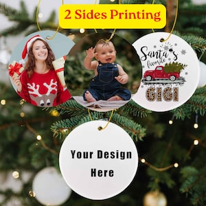 Puede incluir: Cuatro adornos redondos de cerámica colgados en un árbol. Uno muestra a una persona con un suéter de reno, uno a un bebé con overol de mezclilla, uno un camión rojo con el texto Santa's favorite GIGI y uno blanco con el texto Your Design Here.