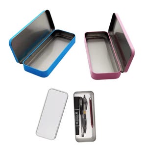 May include: Two rectangular metal pencil cases with hinged lids, one in bright blue and one in pink, shown open. Below, a silver-toned metal case is shown closed next to an open one containing a black marker, two pens, and a red pencil.