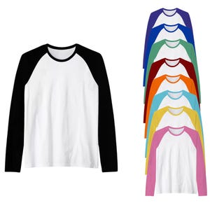 May include: A white long-sleeved baseball tee with black sleeves and collar. A stack of similar shirts in various colours, including blue, green, and pink, are also shown, all with white bodies and coloured sleeves.