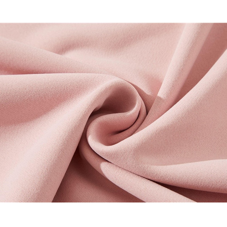 May include: Close-up of a soft, blush pink fabric. The material is tightly woven with a subtle texture, and it is draped in gentle folds, creating shadows and highlights. The fabric appears smooth and luxurious.